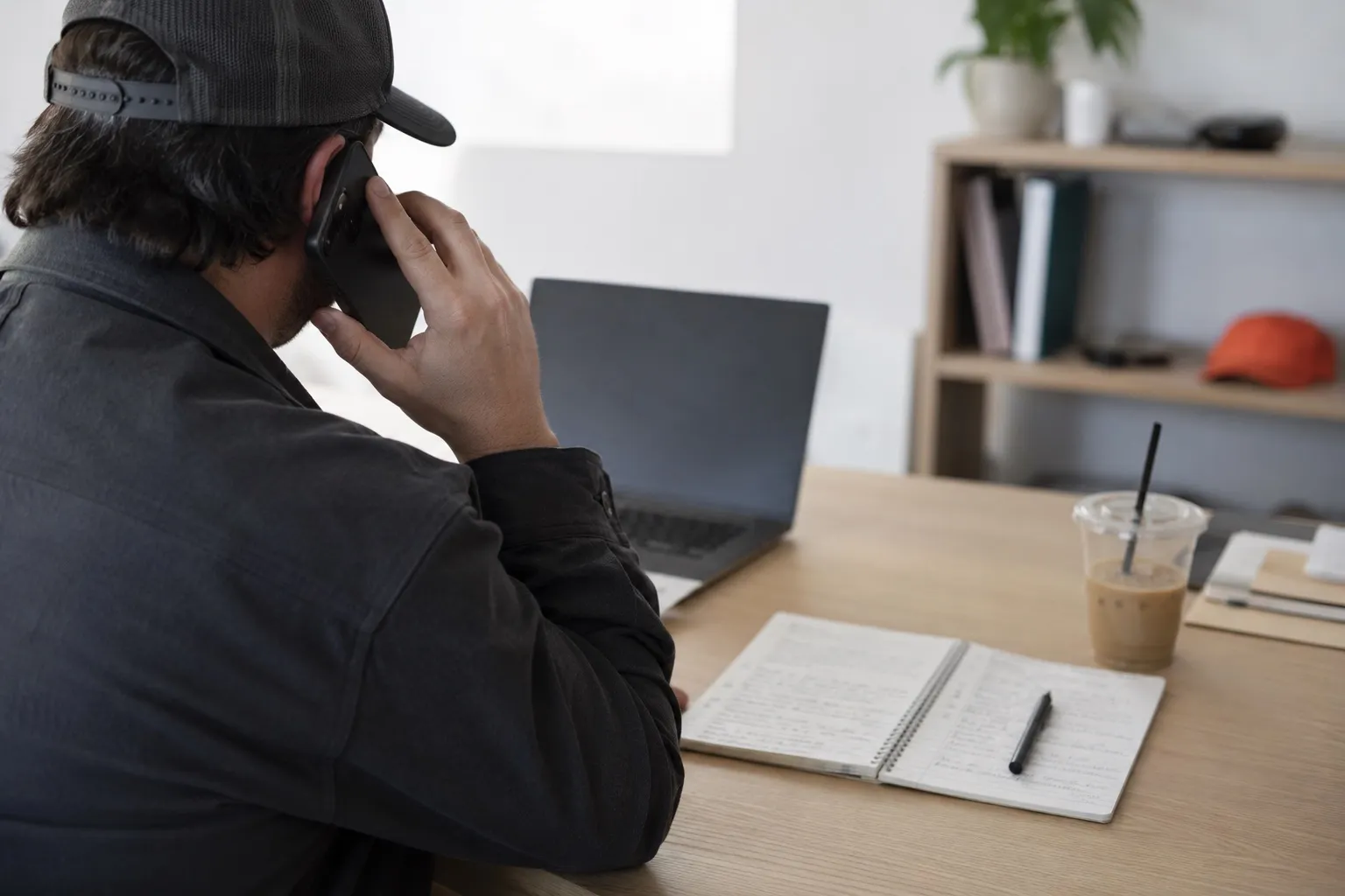 An agency founder on a call at their desk, a handwritten call list open beside a closed laptop